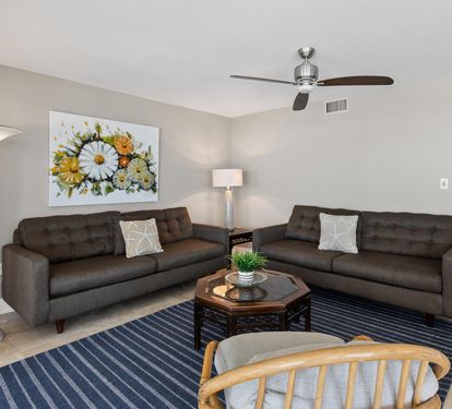 Relax in your spacious living room featuring plush seating, cheerful artwork, and gentle ceiling fan comfort for perfect temperature control.