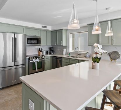 Your modern sage-green kitchen welcomes culinary adventures with gleaming countertops, stainless steel appliances, and pendant lights casting a warm glow over your island workspace.