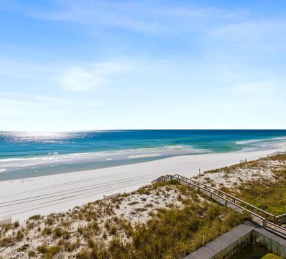 Pristine white sand beach stretches along turquoise waters with dunes and boardwalk access nearby.