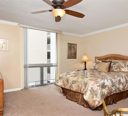 Sleep peacefully in your tropical-themed bedroom with a queen bed, ceiling fan, and natural light from large windows.