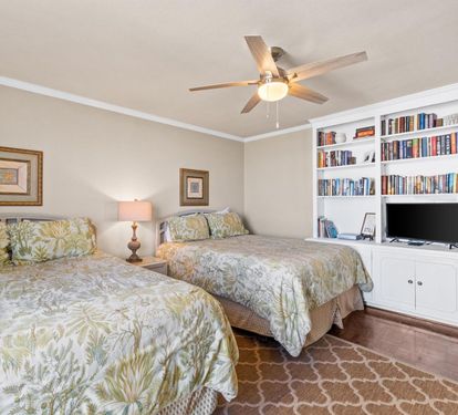 Unwind in your peaceful twin bedroom, featuring built-in shelving, entertainment center, and tropical bedding for ultimate comfort.