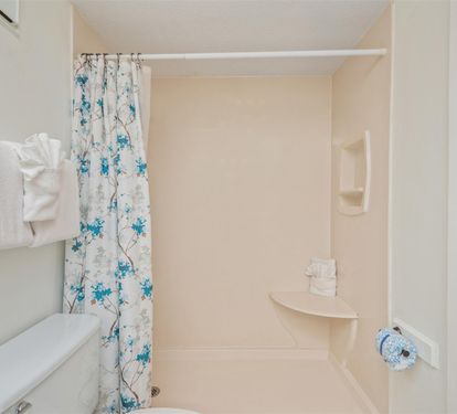Step into your private bathroom with a spacious shower, fresh towels, and cheerful floral curtain for complete comfort.