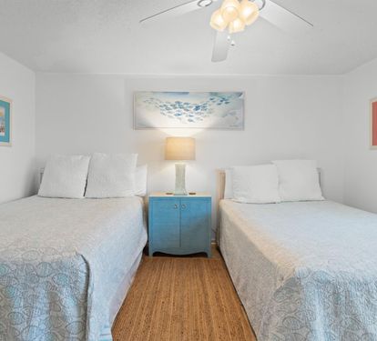 Your twin beds offer fresh linens and ocean artwork, perfect for peaceful nights with the ceiling fan's gentle breeze.