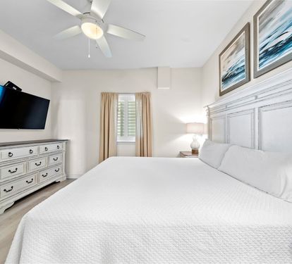 Drift off in this peaceful bedroom featuring crisp white linens, coastal artwork, and a gentle ceiling fan creating your perfect sleep sanctuary.