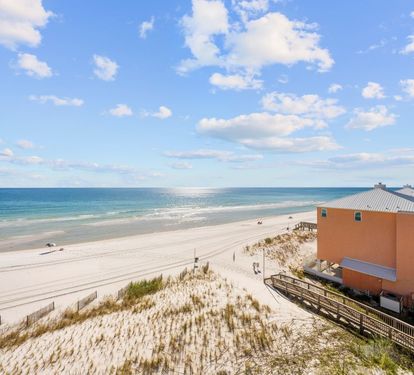 Stunning beachfront view showcasing pristine white sand, turquoise waters, and neighboring coastal buildings under a brilliant blue sky.