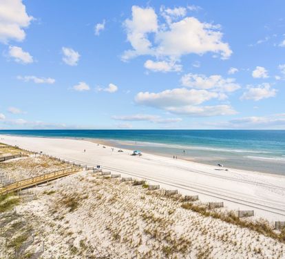 Pristine white sand beach stretches along crystal-clear waters under blue skies dotted with fluffy clouds.