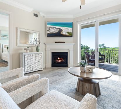 Step into your bright, coastal-chic living room where plush seating and a cozy fireplace invite you to relax after sun-soaked days. Large windows frame your private balcony views of endless greenery.