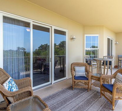Covered balcony provides a comfortable retreat with wicker seating, bistro table, and peaceful treetop views stretching into the distance.