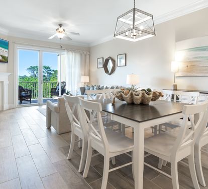 Your open-concept living and dining area features coastal elegance with a cozy fireplace, ocean-view balcony access, and seating for eight beneath soft lighting, perfect for relaxed evenings together.