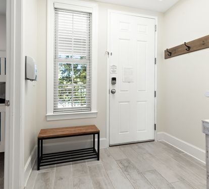 A bright entryway greets you with coastal charm—wooden hooks for beach bags, a bench for sandy feet, and glimpses of a cozy bunk room ready for family fun.