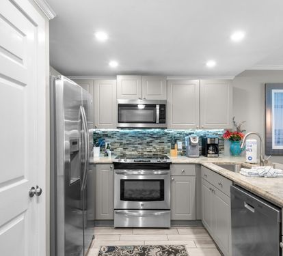 A bright, well-appointed kitchen with coastal flair—stainless steel appliances, a mosaic tile backsplash in cool blues, and plenty of counter space for making memories.