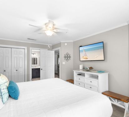 Relax in your peaceful bedroom with plush white linens, coastal accents, and a ceiling fan to keep you cool on warm evenings.