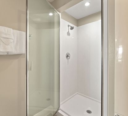 Step into the private glass-enclosed shower with fresh white tiles and plush towels ready for your comfort.