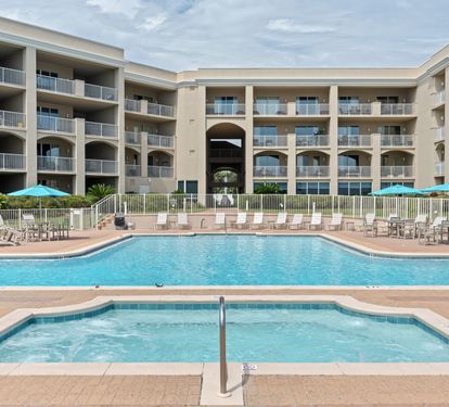 Beachfront resort featuring a sparkling pool, hot tub, and multiple balconies under sunny skies—your coastal retreat awaits.