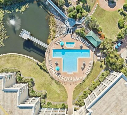 Aerial view showcasing the resort's distinctive cross-shaped pool, surrounded by lush gardens, waterfront access, and modern accommodations—a tranquil retreat nestled between green lawns and natural water features.