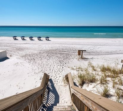 Private boardwalk leads directly to pristine white sand beach and crystal-clear turquoise waters under sunny skies, offering easy access to your coastal escape.