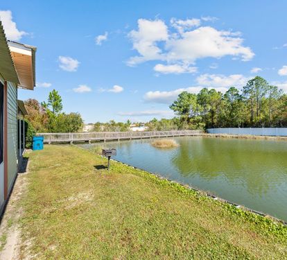 Waterfront property featuring a peaceful lake with walking bridge and lush natural surroundings under bright blue skies.
