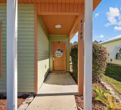 A bright welcome awaits at this cheerful cottage entrance with its mint green siding and warm orange accents under sunny Florida skies.