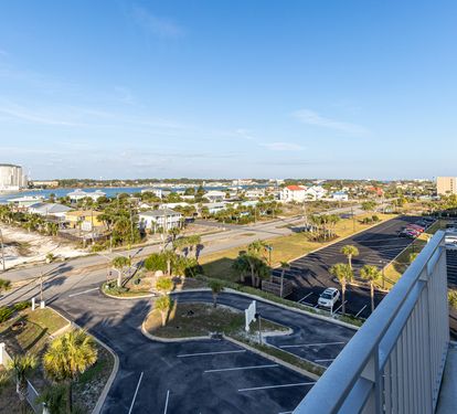Aerial view of coastal area featuring waterfront buildings, palm-lined streets, and nearby bay waters.