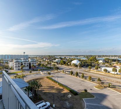 Elevated view showcasing the property's surroundings with coastal buildings, palm trees, and nearby amenities extending toward the horizon.
