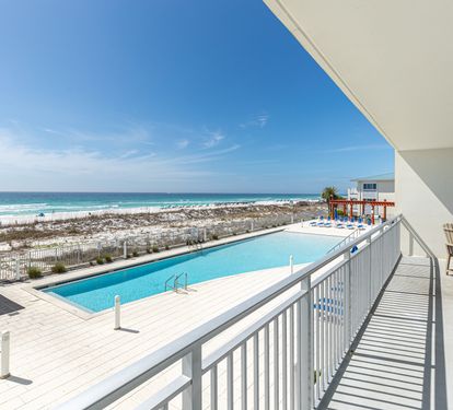 Stunning beachfront balcony with panoramic ocean views, pool access, and outdoor seating overlooking pristine sandy shores.