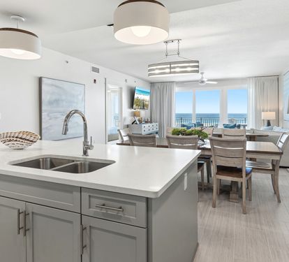 Your modern kitchen island seamlessly flows into the dining area, where ocean views stretch endlessly beyond elegant furnishings.