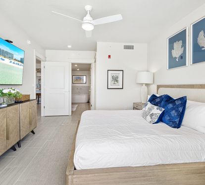 Unwind in your bright coastal bedroom featuring crisp linens, ocean-themed artwork, and a large TV for relaxation.
