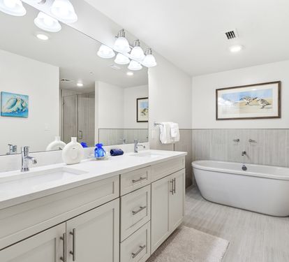 Indulge in your private spa-like bathroom featuring dual sinks, a luxurious soaking tub, and elegant coastal artwork that creates a serene retreat.