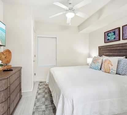 Sink into crisp white linens and coastal-themed pillows in your serene bedroom, where gentle ceiling fan breezes keep you cool.