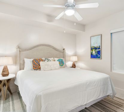 Sink into coastal comfort with crisp white linens, cheerful throw pillows, and a gentle ceiling fan to keep you cool.