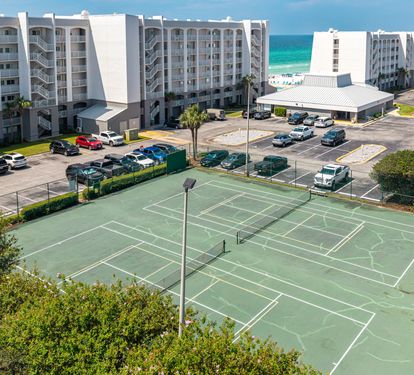 Aerial view of the vacation property featuring tennis courts, ample parking, and proximity to the stunning turquoise Gulf waters and pristine beach.