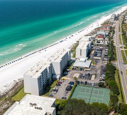 Beachfront property located along pristine white sand beaches with emerald waters of the Gulf. The property features tennis courts, ample parking, and direct beach access with umbrella rentals lining the shore.