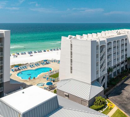 Aerial view showcasing the beachfront resort nestled between pristine white sand and emerald Gulf waters, with pool facilities and coastal access for guests.