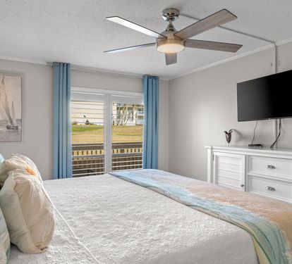 Wake up to peaceful golf course views from the comfort of the primary bedroom featuring a king bed, coastal décor, and direct access to the private patio for a relaxing indoor-outdoor retreat.