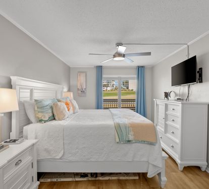 This inviting primary bedroom features a comfortable king bed, coastal-inspired furnishings, and relaxing golf course views just outside. A peaceful retreat designed for comfort, relaxation, and restful nights.
