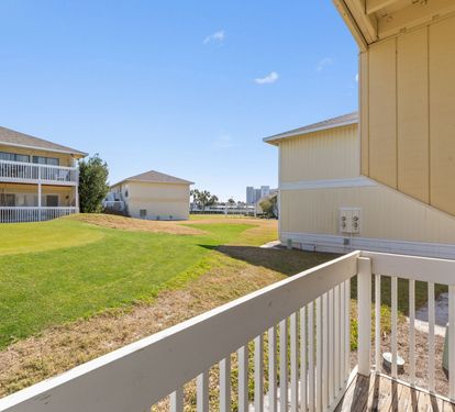 A peaceful residential property with neighboring buildings, open green space, and distant city skyline visible from the balcony.