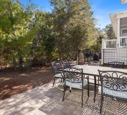 Your private patio awaits with elegant dining furniture surrounded by mature trees, perfect for morning coffee or evening meals in peaceful seclusion.