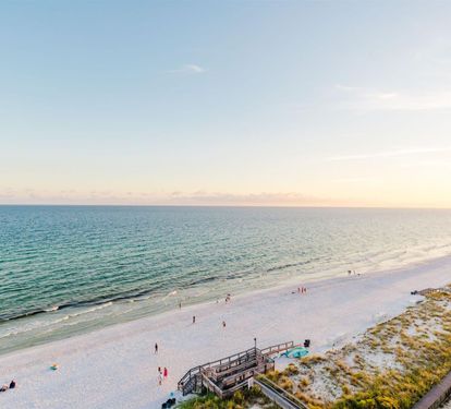Beautiful Gulf Coast beach with pristine white sand and emerald waters stretches along the shoreline during golden hour.