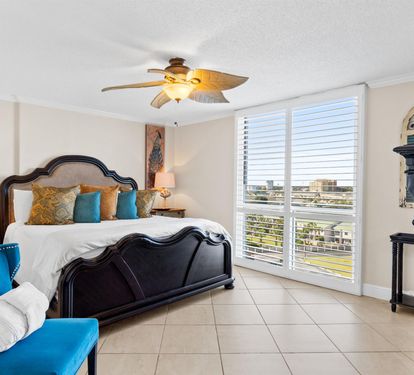 Your elegantly appointed bedroom features a luxurious king bed with vibrant accent pillows, offering peaceful comfort with stunning city views through plantation shutters.