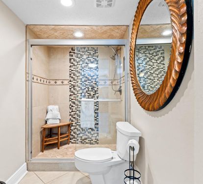 Refresh in your beautifully tiled bathroom featuring a spacious walk-in shower with stunning mosaic accents and convenient bench seating.