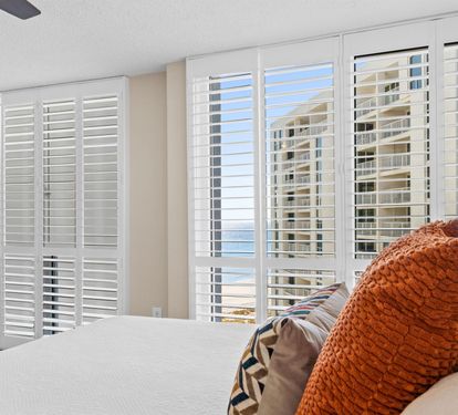 Wake up in this bright bedroom where white shutters frame stunning city views and soft linens invite restful sleep.