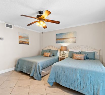 Relax in your coastal-themed bedroom with twin beds, soft ocean-blue linens, and a gentle ceiling fan for comfort.
