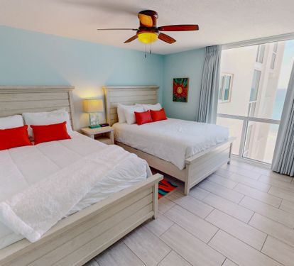 Drift off to sleep in your bright, comfortable bedroom featuring two plush beds with crisp linens and cheerful red accents.