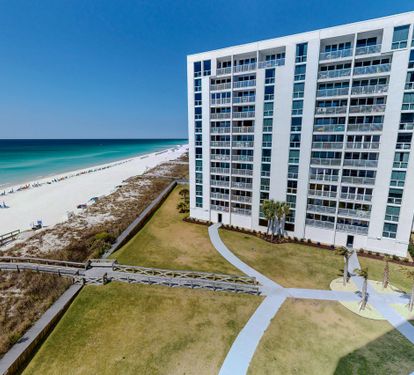 Stunning beachfront high-rise property with direct beach access via wooden boardwalk and manicured grounds.