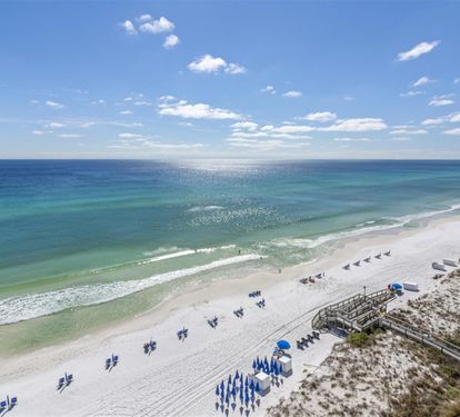 Stunning aerial view of pristine white sand beach with turquoise waters and beachside amenities including umbrellas and boardwalk access.