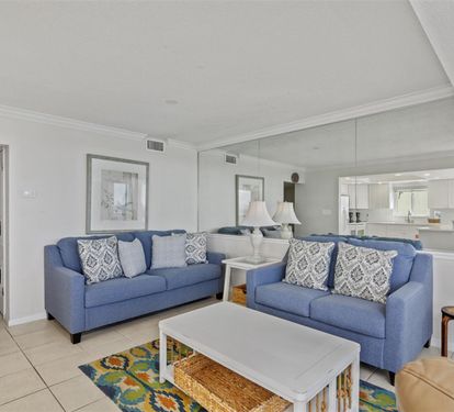 Relax in your spacious living room with comfortable blue sofas and elegant coastal decor, flowing seamlessly into the modern kitchen.