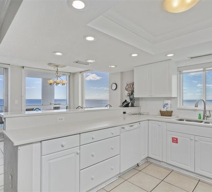 Cook with breathtaking ocean views through floor-to-ceiling windows in your fully equipped kitchen with white cabinetry and modern appliances.