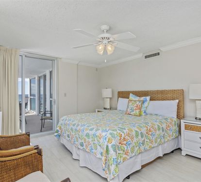 Your bright bedroom features coastal charm with a wicker headboard, tropical bedding, and sliding doors to your private balcony.