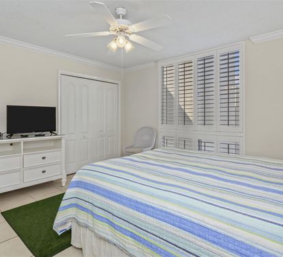 Your peaceful bedroom retreat features a comfy bed with coastal-striped linens, entertainment center, and gentle ceiling fan for ultimate relaxation.