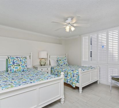 Rest peacefully in this bright twin bedroom featuring coastal-themed bedding, plantation shutters, and a cozy reading chair for quiet moments.